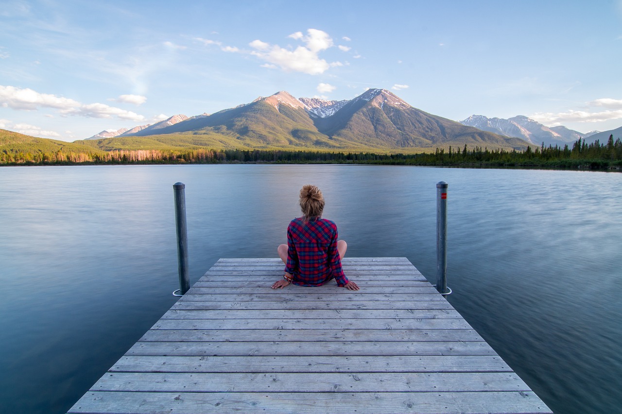 relación real entre mente y cuerpo. El poder de la mente. Foto tomada de un embarcadero con una mujer sentada mirando el horizonte frente a ellas montañas.